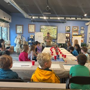 Children gathered around a table during a Junior Cartography Class at Xplorer Maps Headquarters.