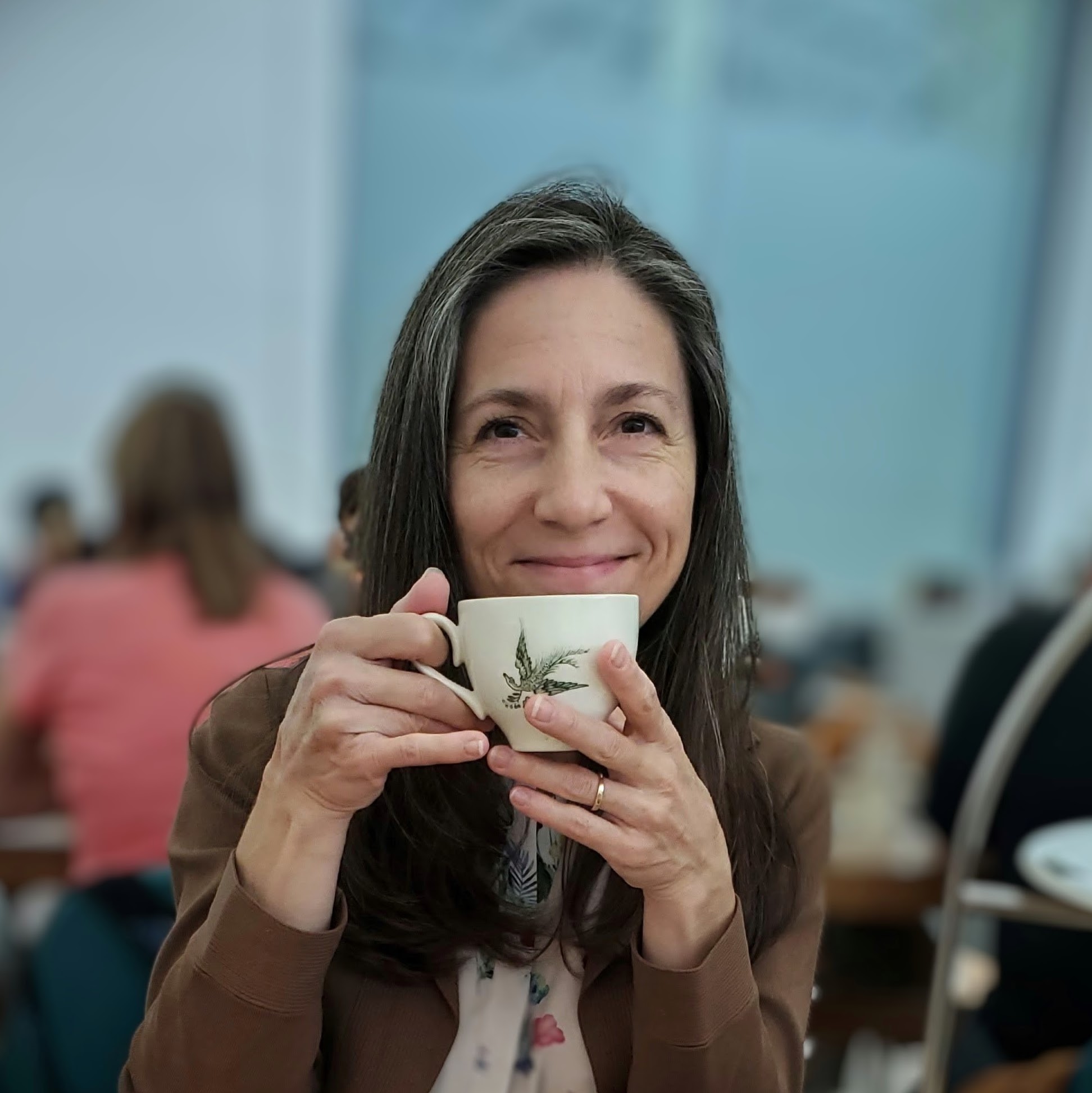 Dark haired woman holding a cup of tea up to her face.